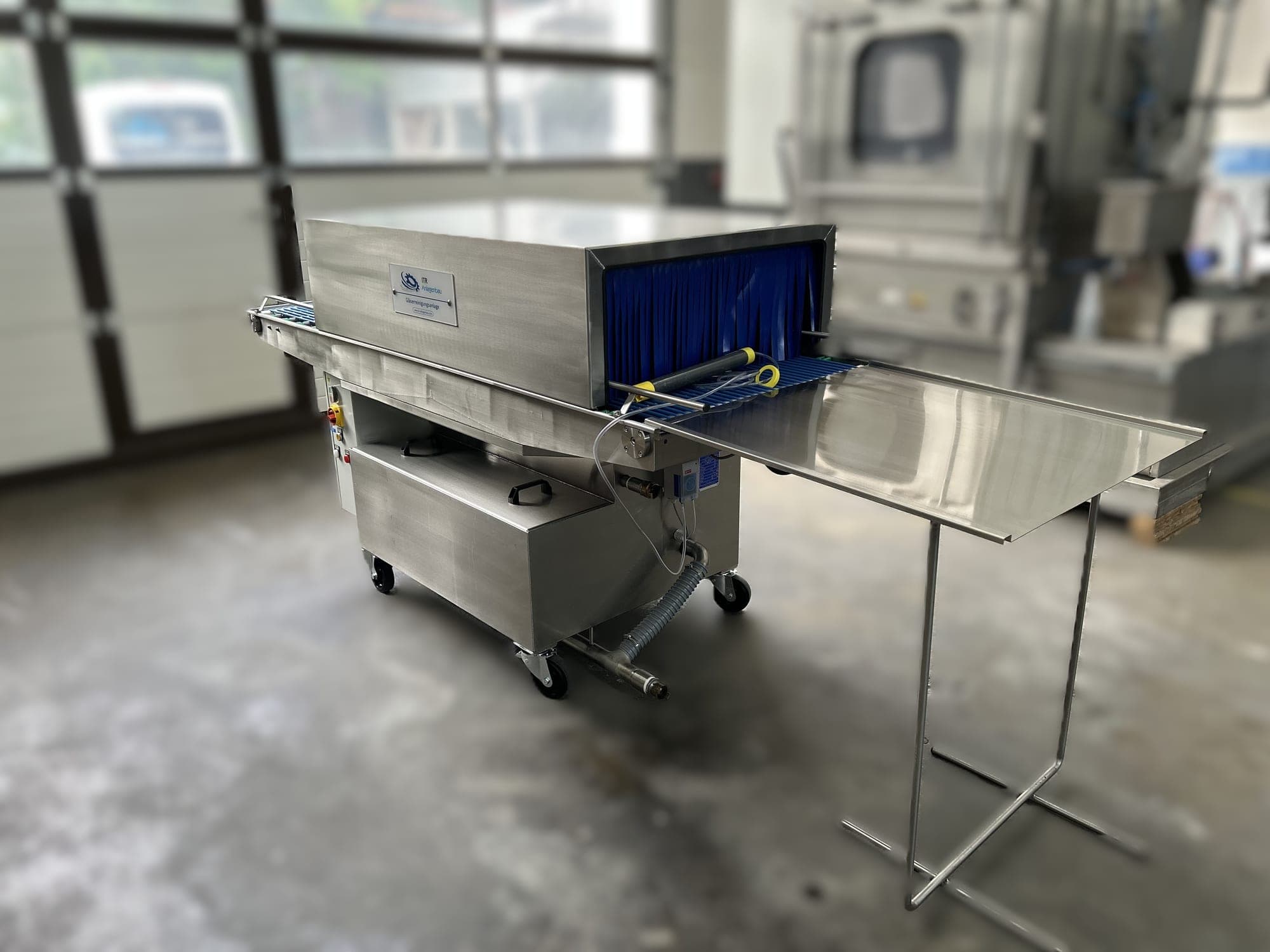 Fahrbare Gläser-Durchlaufreinigungsanlage aus Edelstahl mit blauem Lamellenvorhang am Einlauf und angesetztem Ablauftisch